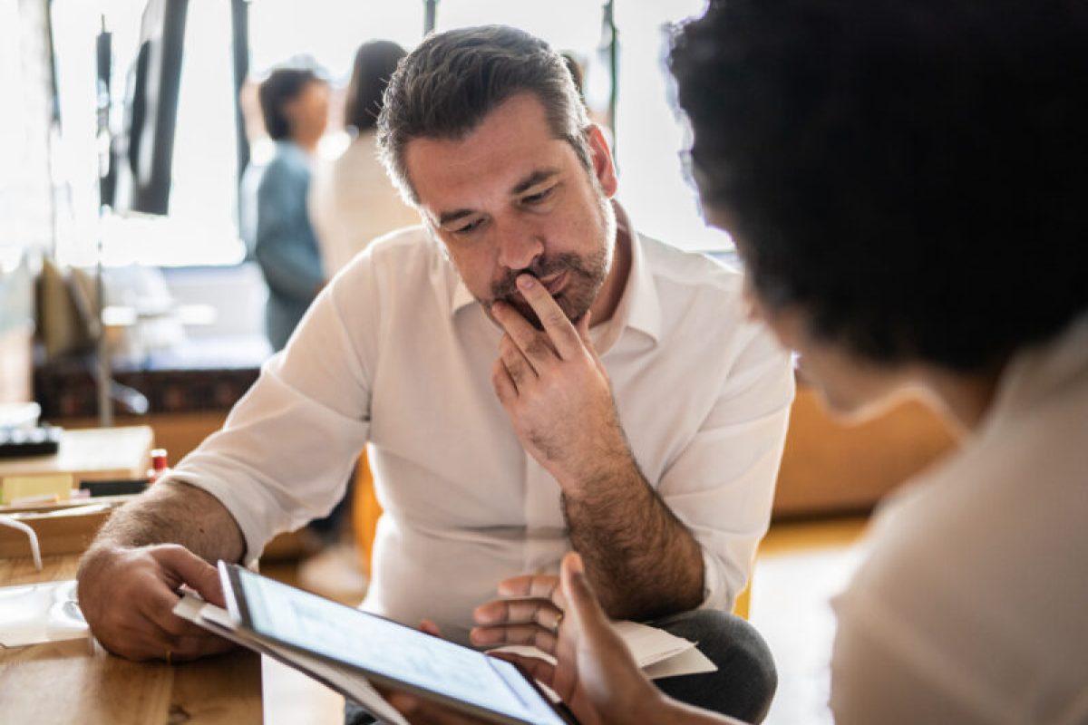 Mature man looking at a digital tablet that a colleague is showing at work Mature man looking at a digital tablet that a colleague is showing at work