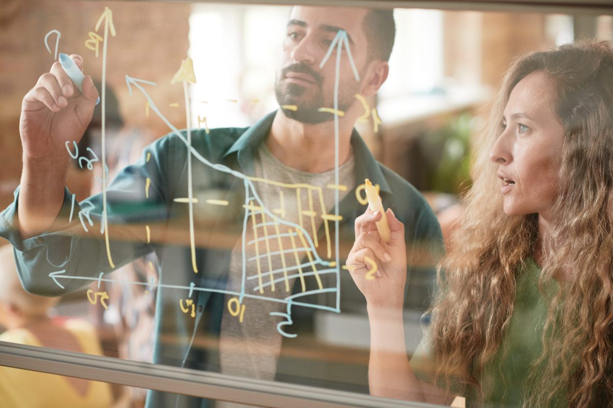 Business people examining graphics at office Business colleagues drawing financial graphic on glass wall and examining it together in team during presentation at office