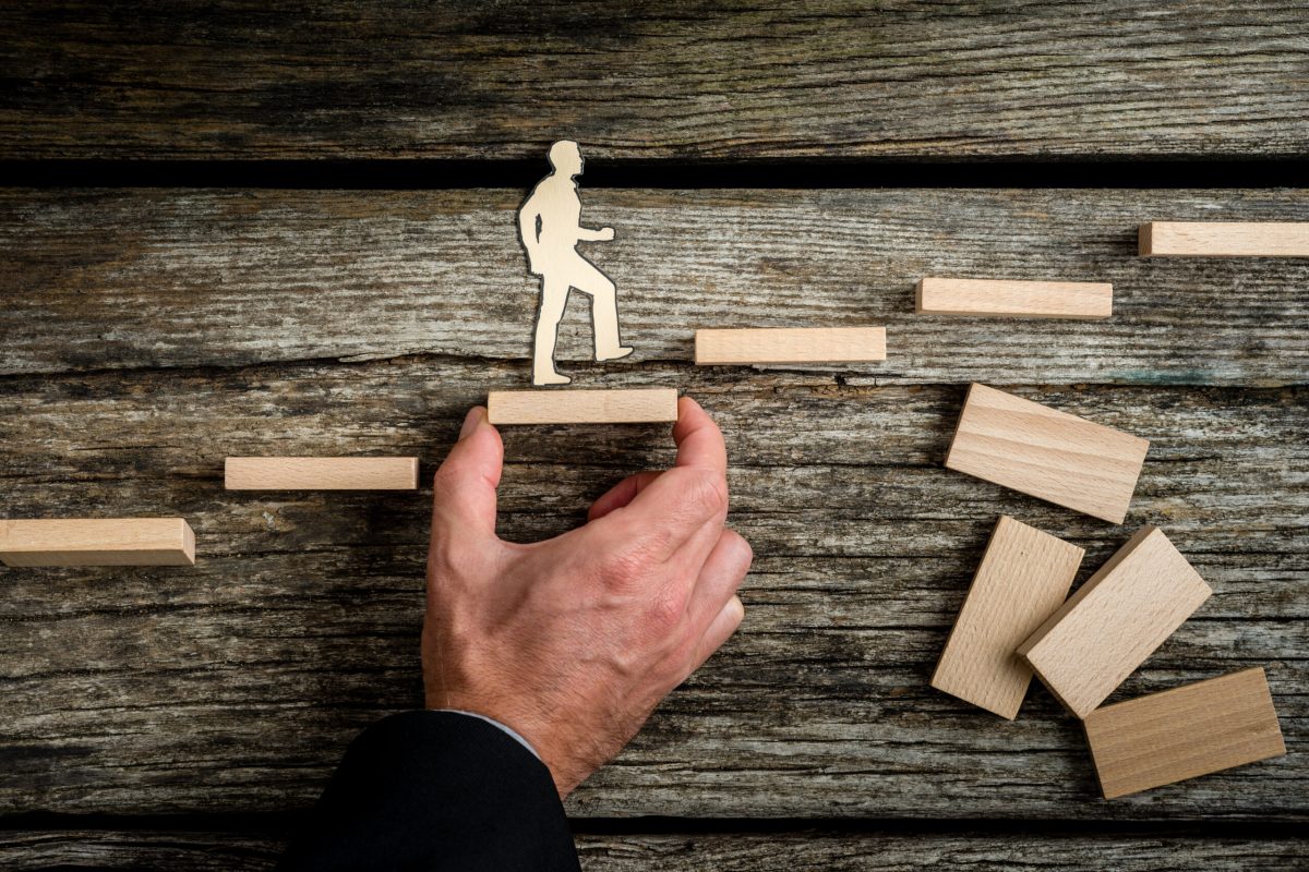 Teamwork concept with businessman holding up stairs Teamwork concept with businessman holding up stairs so that the paper man can walk across over rustic wood.