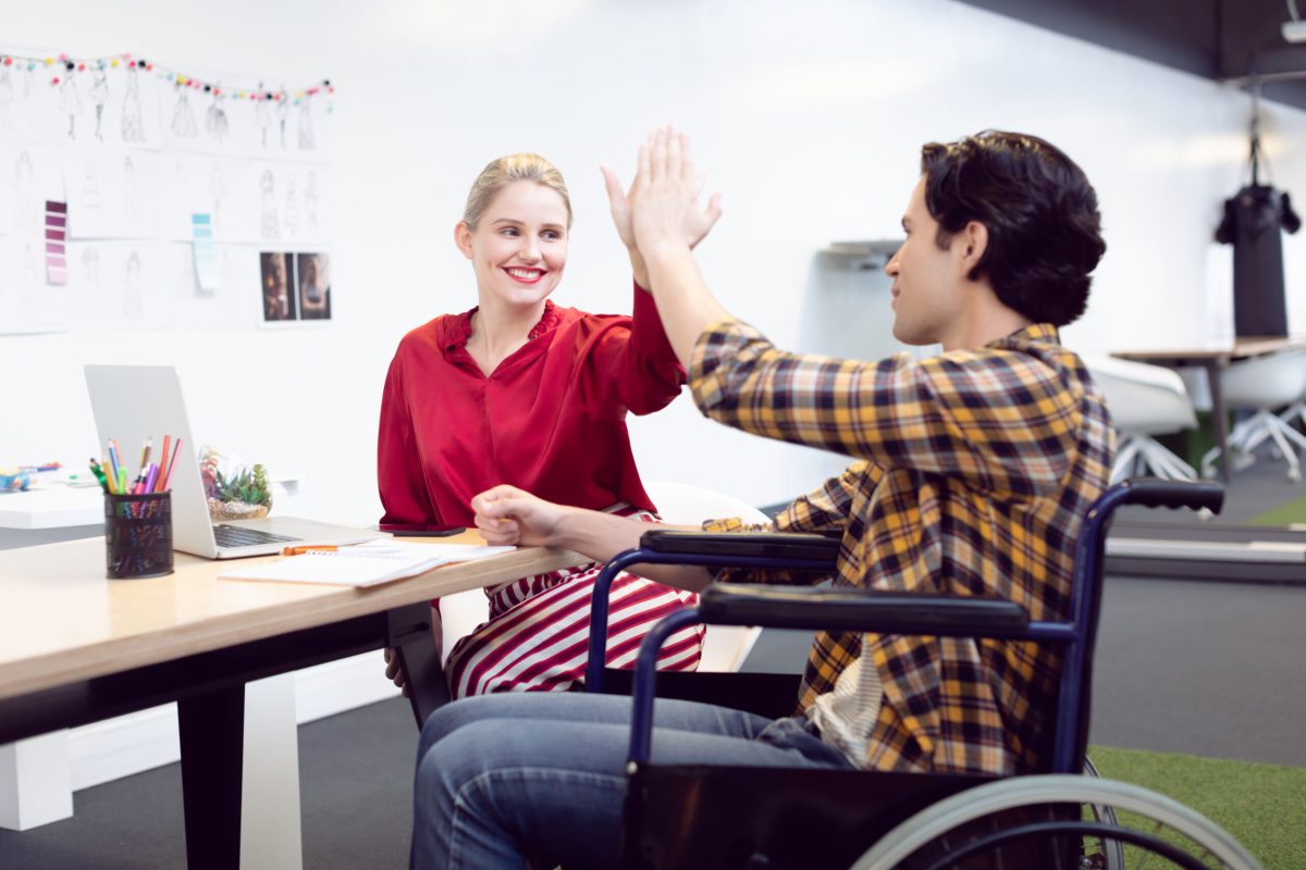 Side view of Caucasian male and female fashion designer giving high five to each other at desk in office