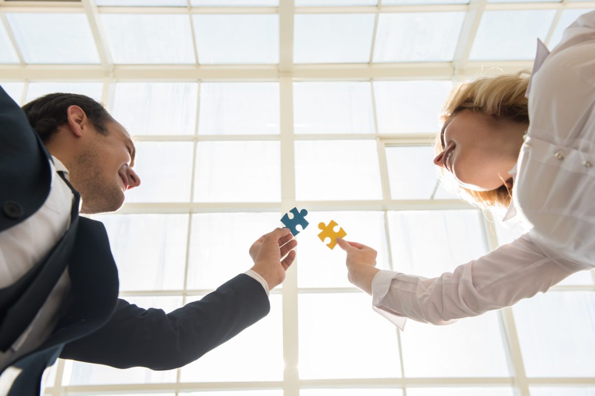 Man and woman joining jigsaw pieces of puzzle in office. Man and woman joining jigsaw pieces of puzzle in office.